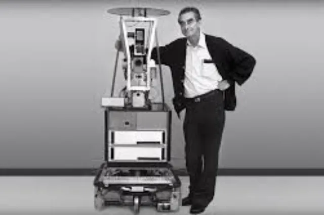 Charles Rosen seated or standing near Shakey, a wheeled robot with a camera and antenna mounted on a tall body
