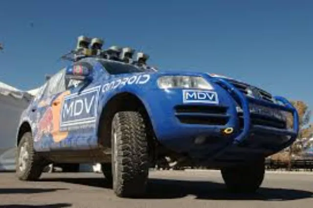 A modified Volkswagen Touareg SUV fitted with a roof-mounted sensor array driving on a desert road