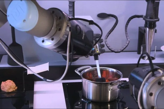 Pair of robotic arms positioned over a kitchen counter with an oven, hob, and sink visible