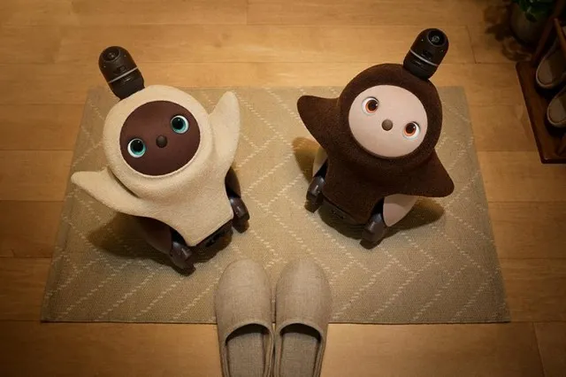 A small round-bodied robot with large eyes and short stubby limbs, held or displayed at a product event