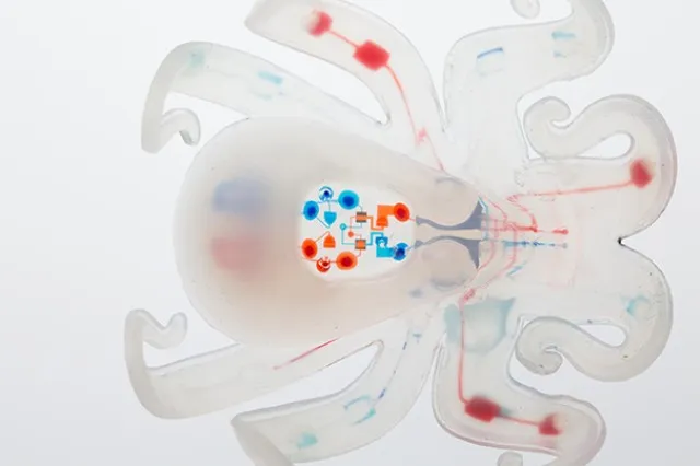 A small translucent soft robot shaped like an octopus with eight extended arms, photographed against a plain background