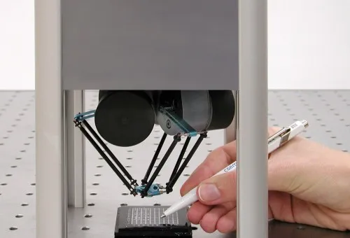 Small parallel delta robot with three arms meeting at a central platform above a work surface