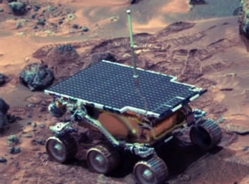 The Sojourner rover on a rocky Martian surface, with reddish terrain and the Pathfinder lander visible nearby